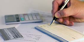 A hand writing a check with a pen next to a calculator