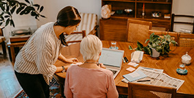 Granddaughter standing helping her sitting grandmother fill out paperwork